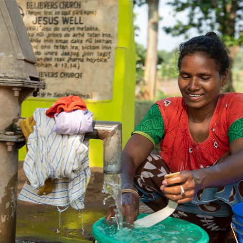 Woman washes clothes with clean water through GFA World Jesus Well