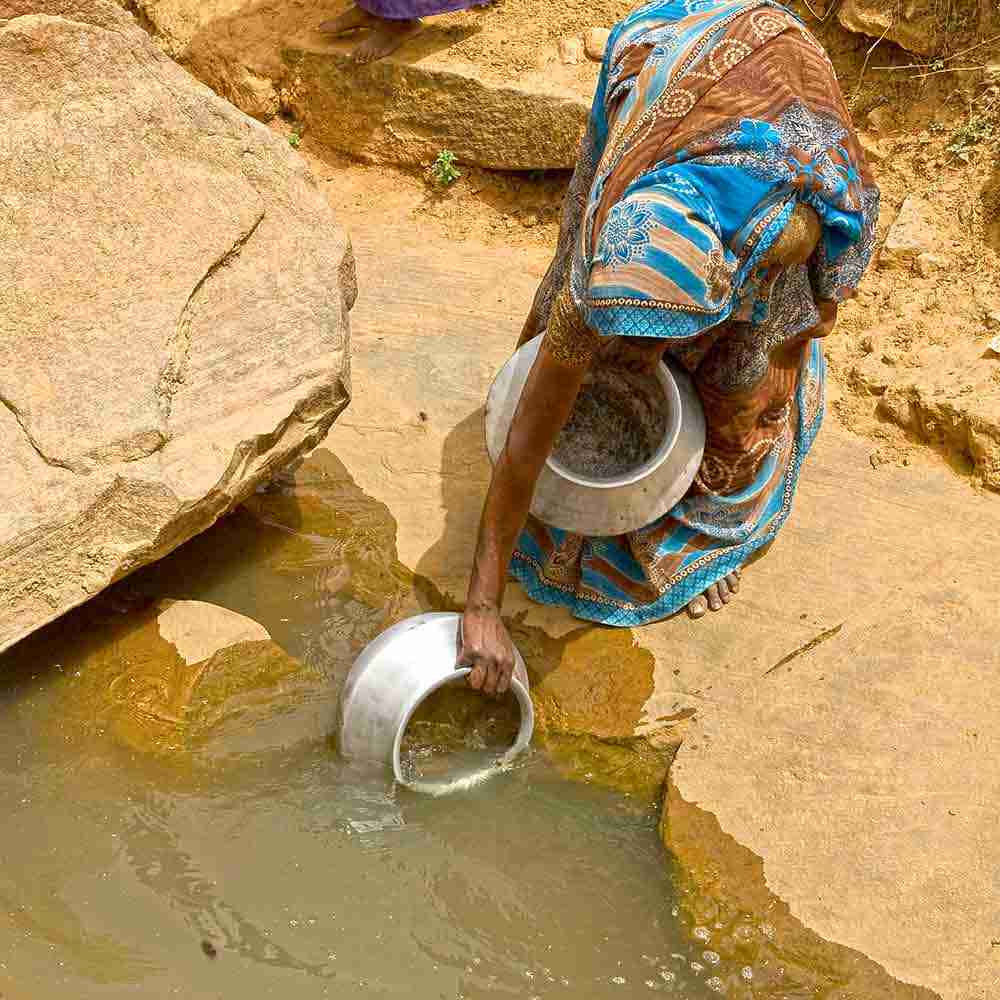 Woman drawing water from a contaminated open water hole