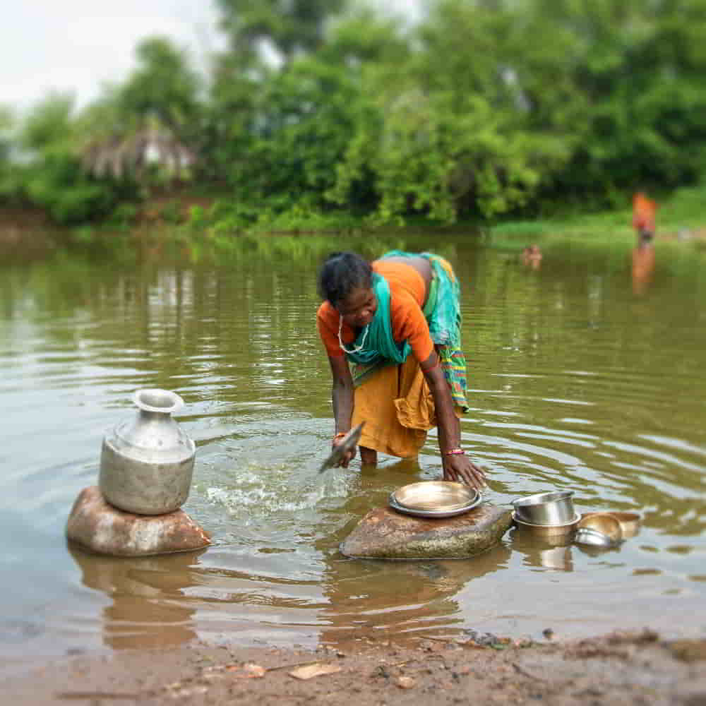 Woman washing pots and pans using unclean water from a local river