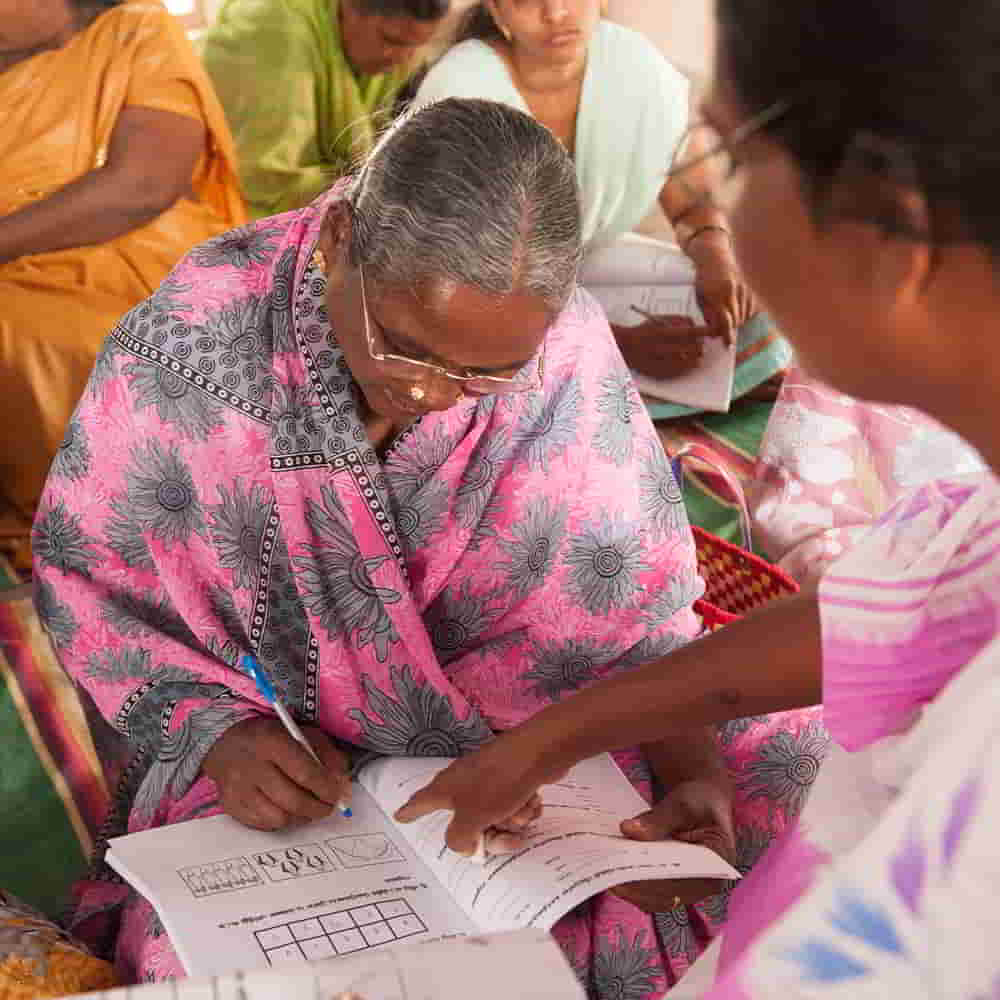 Woman missionary teaches elderly woman in adult literacy class