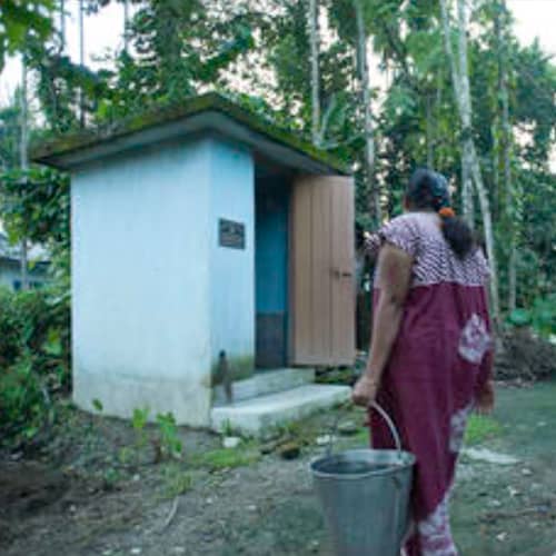 Woman walking toward a GFA World provided outdoor toilet
