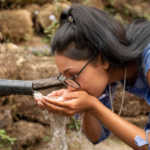 Young woman from Nepal drinks clean water through GFA World Jesus WElls